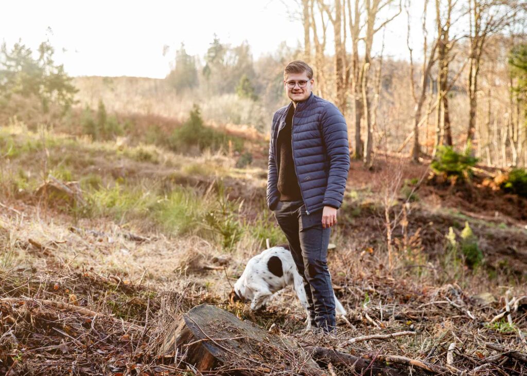 Mediendesigner, Julian Meyer von der Werbeagentur die medienvilla steht im Wiehengebirge auf einer Aufforstungsfläche mit einem Hund